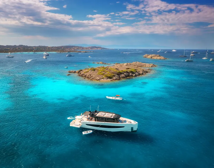 Yacht vor einer winzigen Insel in klarem blauem Wasser, von oben gesehen