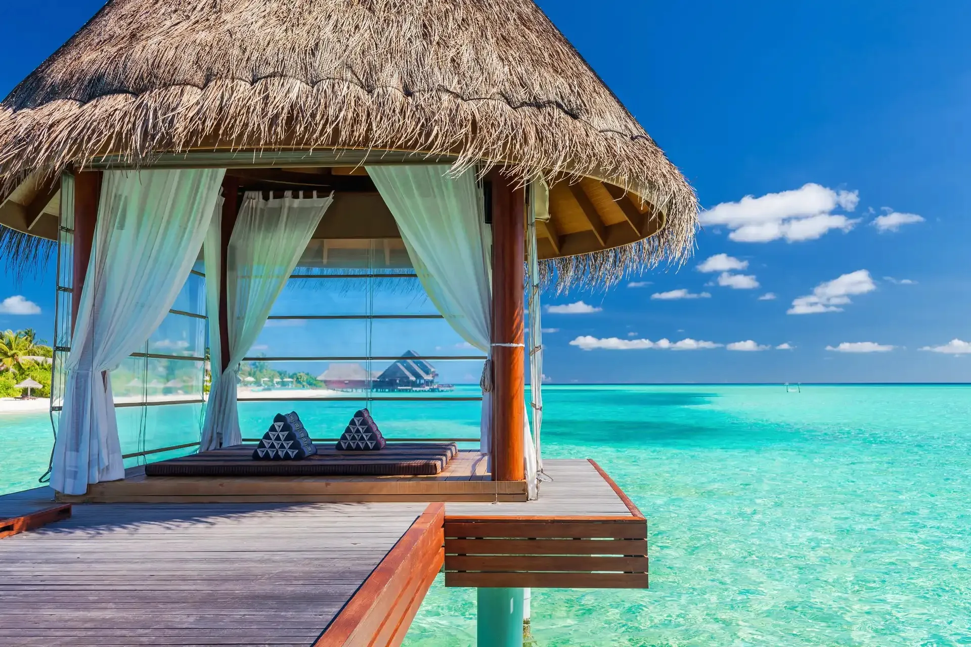 Overwater-Pavillon mit Strohdach und weißen Vorhängen über einer türkisfarbenen Lagune