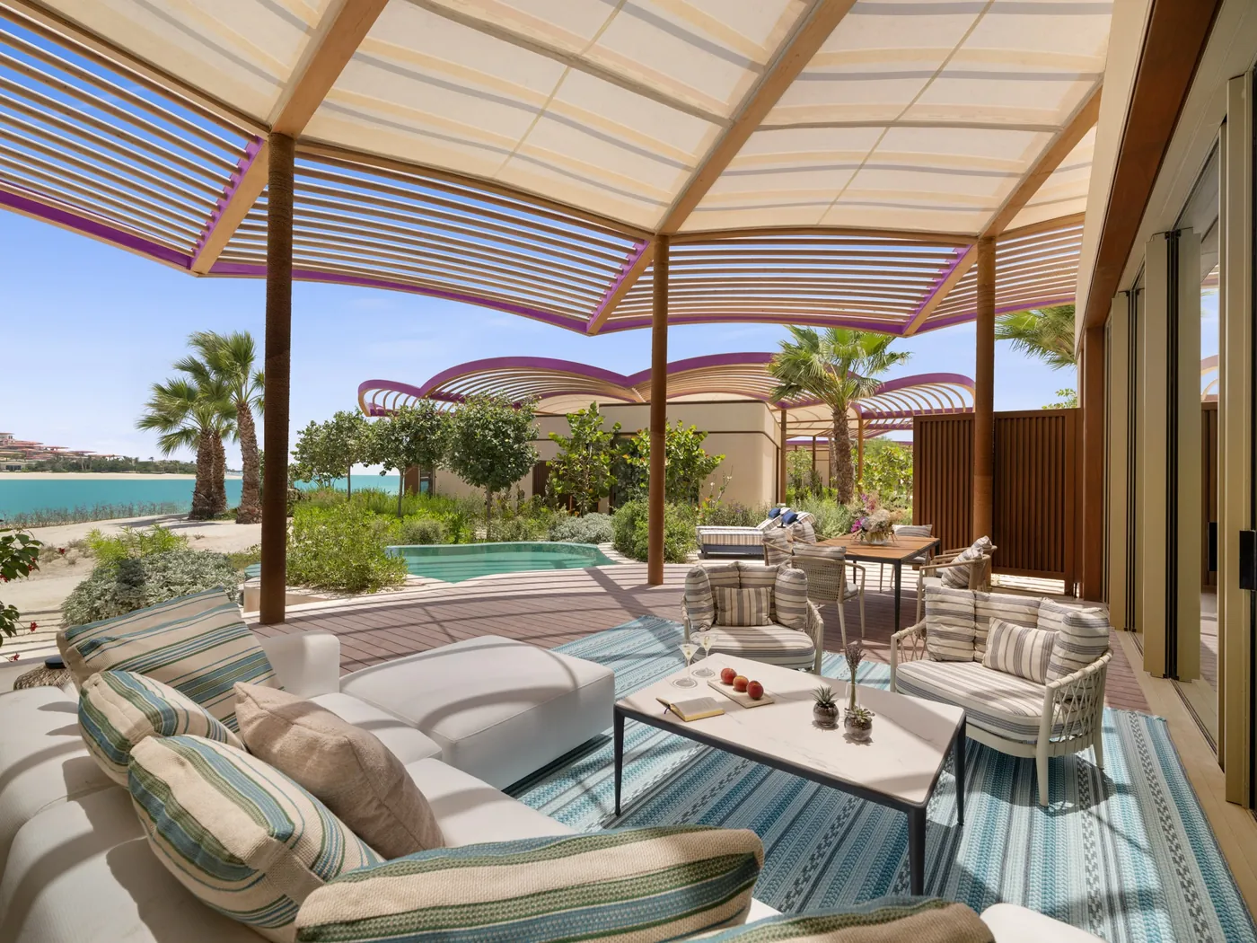 Schattige Terrassen-Lounge mit gestreiften Kissen im Raffles The Red Sea, dahinter ein Pool und Palmen