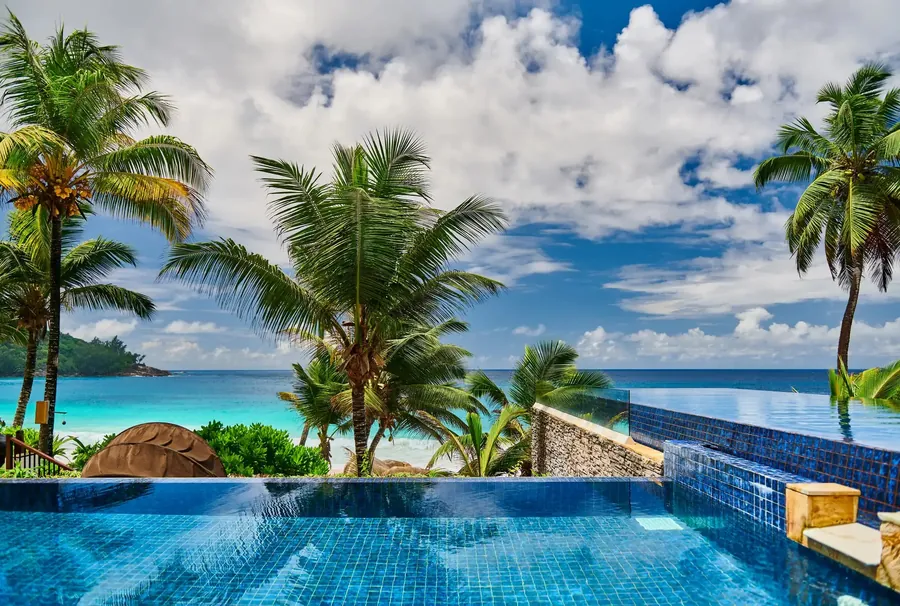 Resortpool zwischen Palmen und Granitfelsen über einem Strand der Seychellen
