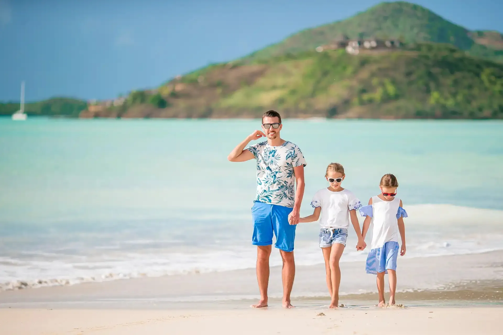 Ein Vater geht Hand in Hand mit zwei Töchtern über einen weißen Strand